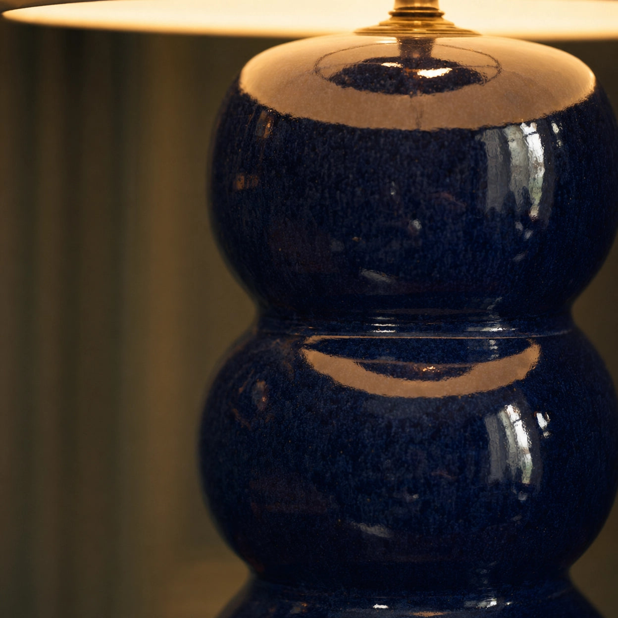 Detail of the Cosmati ceramic base — stacked bobbins in deep indigo high-gloss glaze, showing the bobbin form, brass collar, and warm reflected lamp light