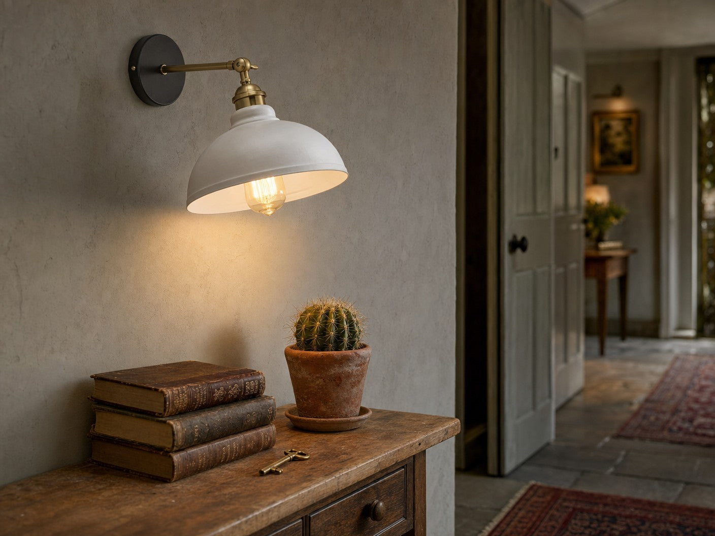 Aldgate adjustable industrial dome wall sconce in white, mounted on chalky plaster wall above an oak hallway console with antique books and brass key, lit by warm Edison bulb