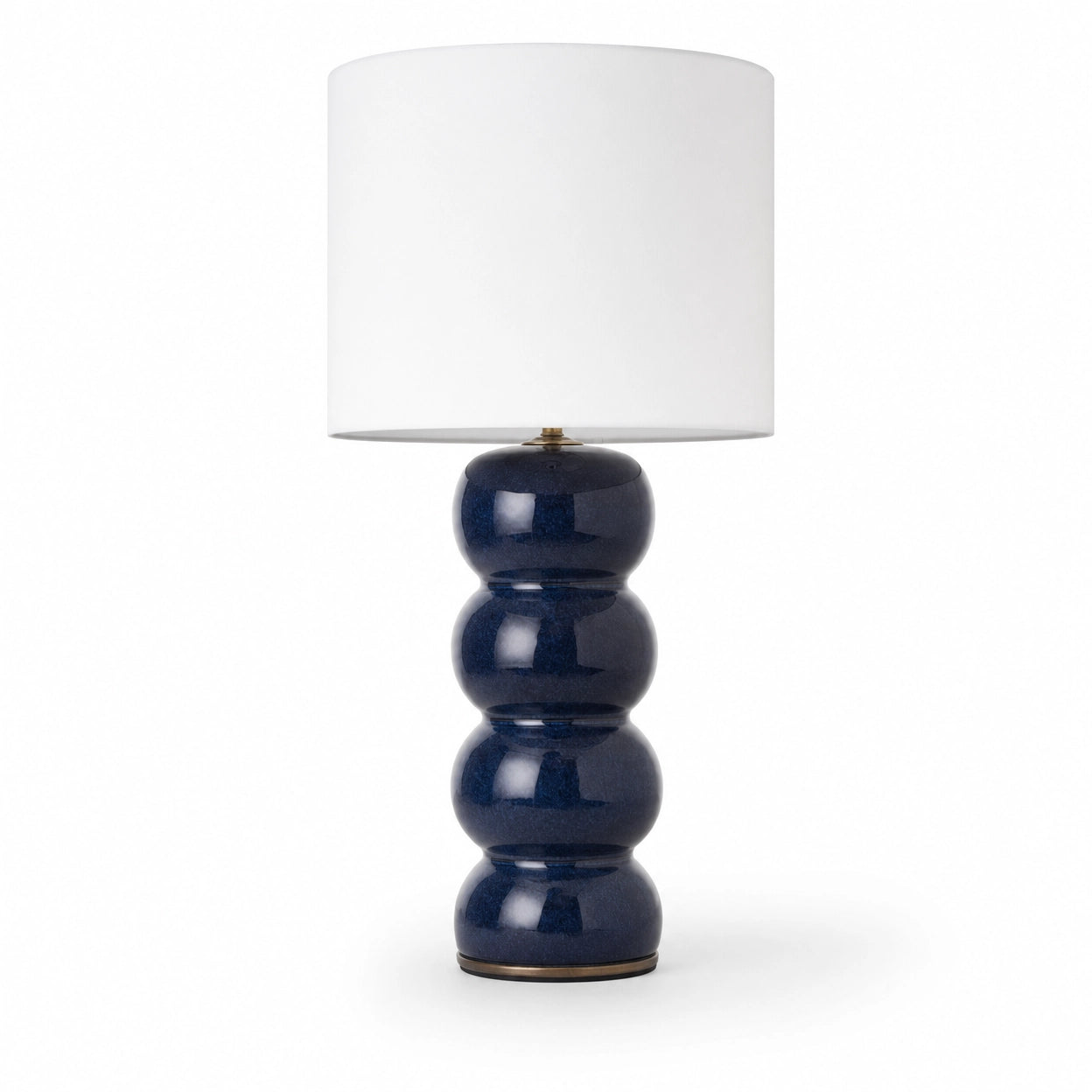 Cosmati bobbin ceramic table lamp on white background — stacked rounded ceramic forms in indigo high-gloss glaze beneath a crisp white drum shade