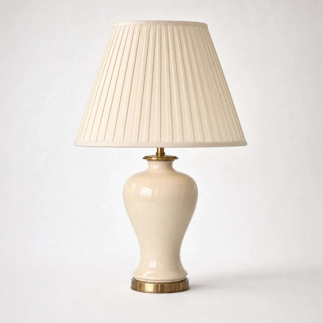 Salcombe table lamp on a soft warm-white background — full 56cm product view of the cream-glazed ceramic urn body on its antique-brass base plate beneath a tall classic empire-form shade in cream knife-pleated silk