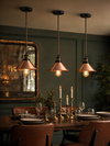 Three Wapping copper pendant lights hanging in a row above a dark wood dining table