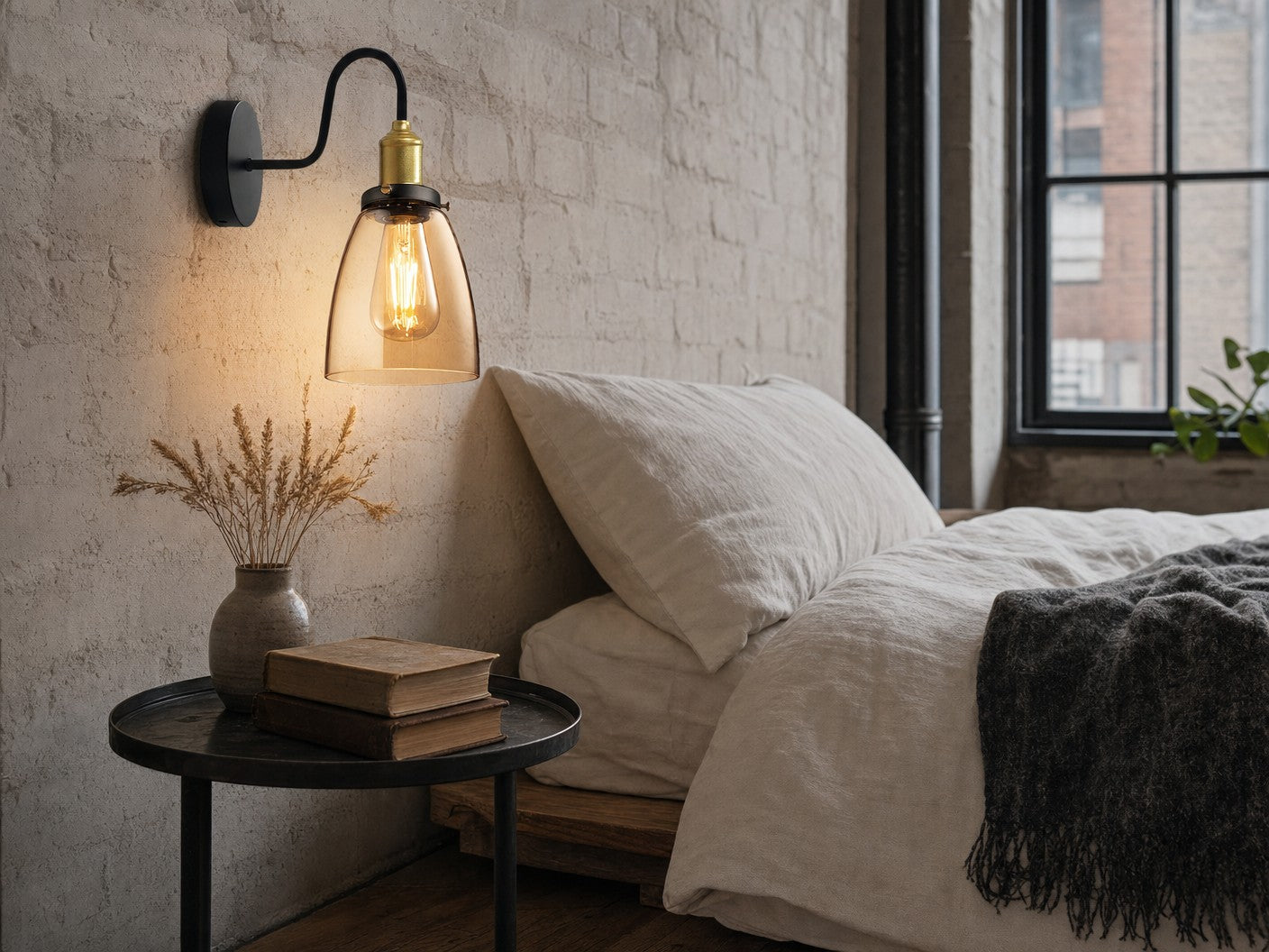 Whitechapel amber-glass gooseneck wall sconce mounted on a chalky off-white limewashed brick wall beside a low platform bed in a Victorian-warehouse-conversion bedroom